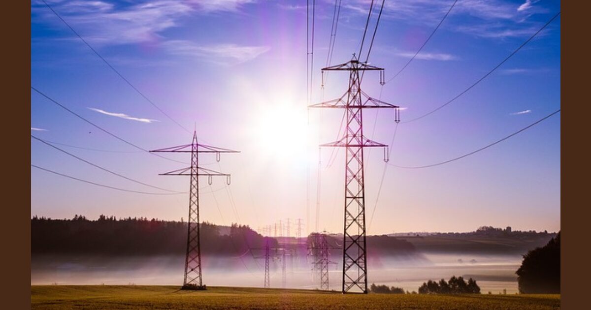 高圧電線の柱が2本立っている。背景に朝日が注ぎ込む。